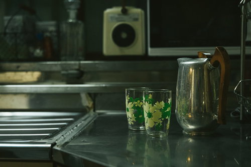 昭和の台所に置かれたステンレス製ポットと緑色のコップ