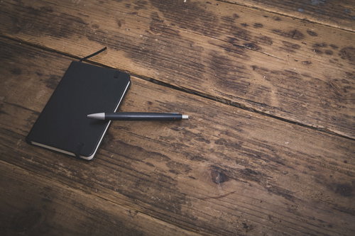 木目のフローリングに置かれた手帳とボールペン