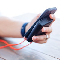 手のひらサイズのモバイルバッテリーとスマートフォン、紅白ボールストラップの写真