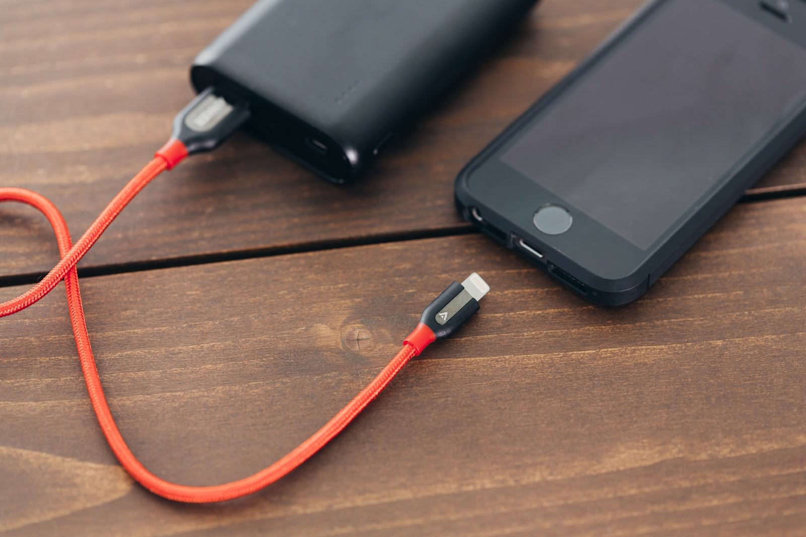 モバイルバッテリーと赤いケーブルで充電中のスマホ