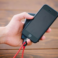 赤いケーブルで接続したモバイルバッテリーを片手で持つスマホの写真
