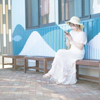 ベンチに座ってスマホで調べ物をする白いシャツの女性の写真