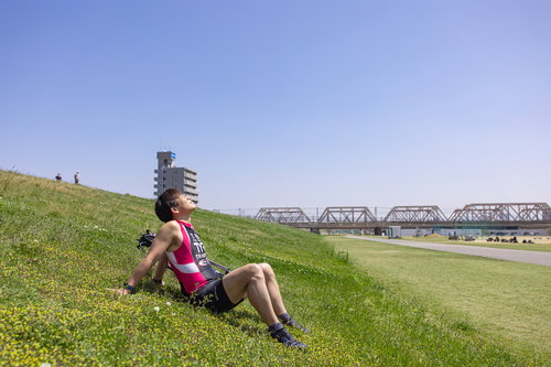 河川敷の芝生で青空を見上げるトライアスロン選手
