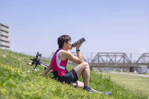 河川敷で休みながら水分補給をするトライアスロン選手の男性