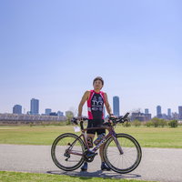 青空の公園で競技用バイクとともにポーズを取るトライアスロン選手の写真