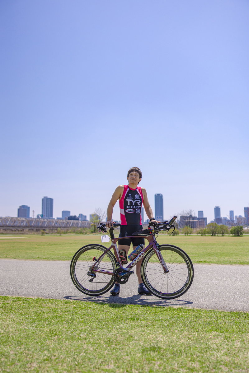 青空の下でバイクと一緒にポーズを取るトライアスロン選手［モデル：うえせい］