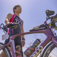 炎天下の中でロードバイクと共にポーズを決めるトライアスロン選手の写真