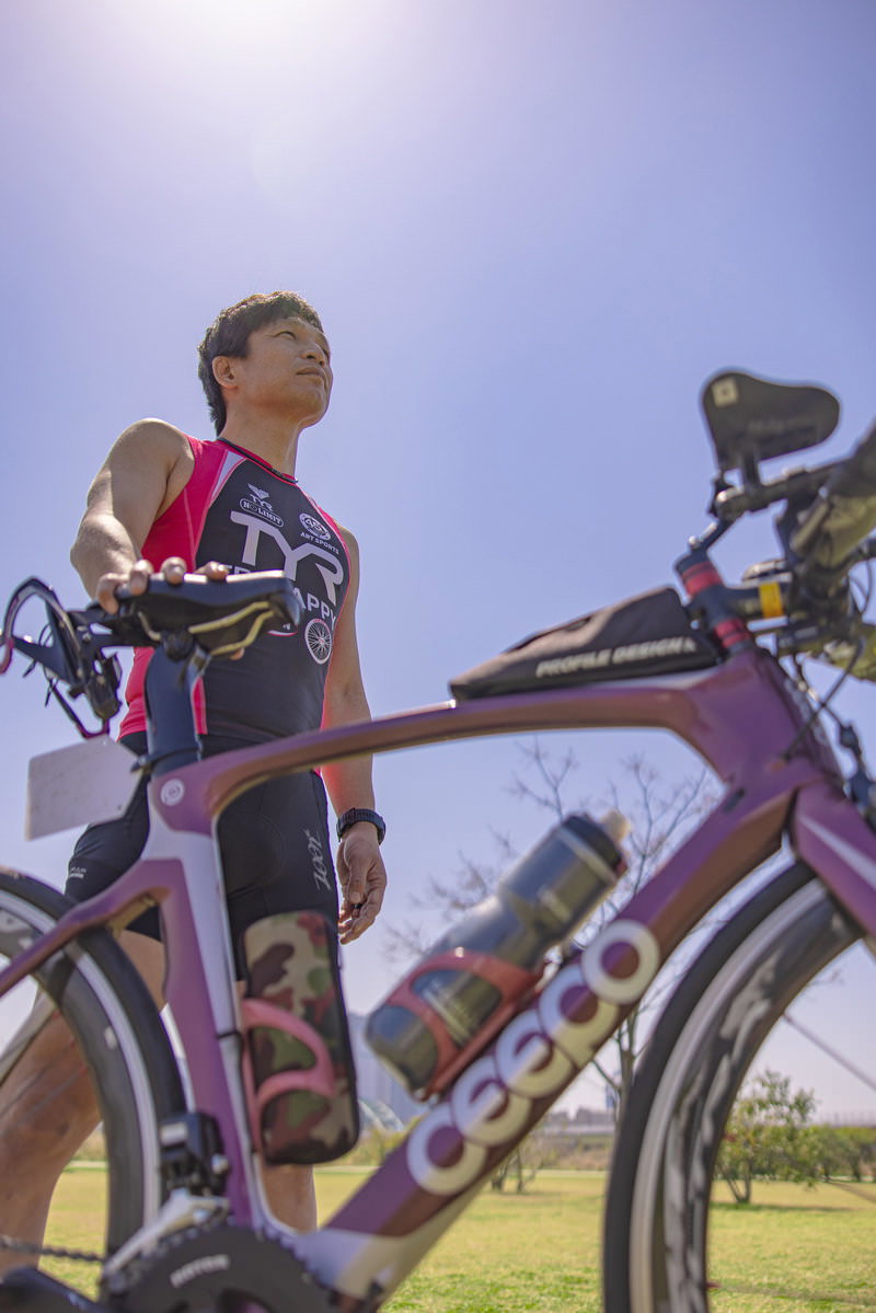 炎天下の青空の下でロードバイクと共にポーズを決めるトライアスロン選手［モデル：うえせい］