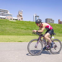 河川敷を走行するロードバイカー、ピンクのウェア姿で力強く駆け抜けるの写真