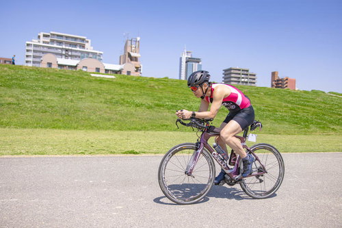 河川敷を走行するロードバイカー、ピンクのウェア姿で力強く駆け抜ける