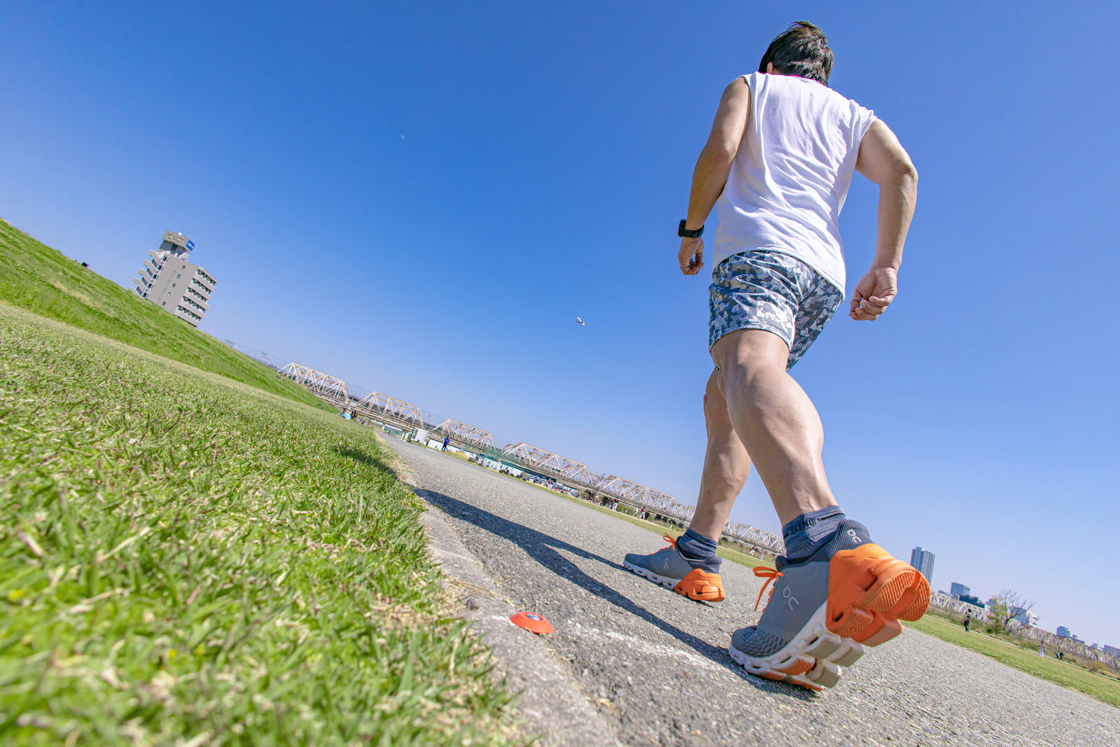 アスファルトの道路をランニングする男性の足元と影［モデル：うえせい］