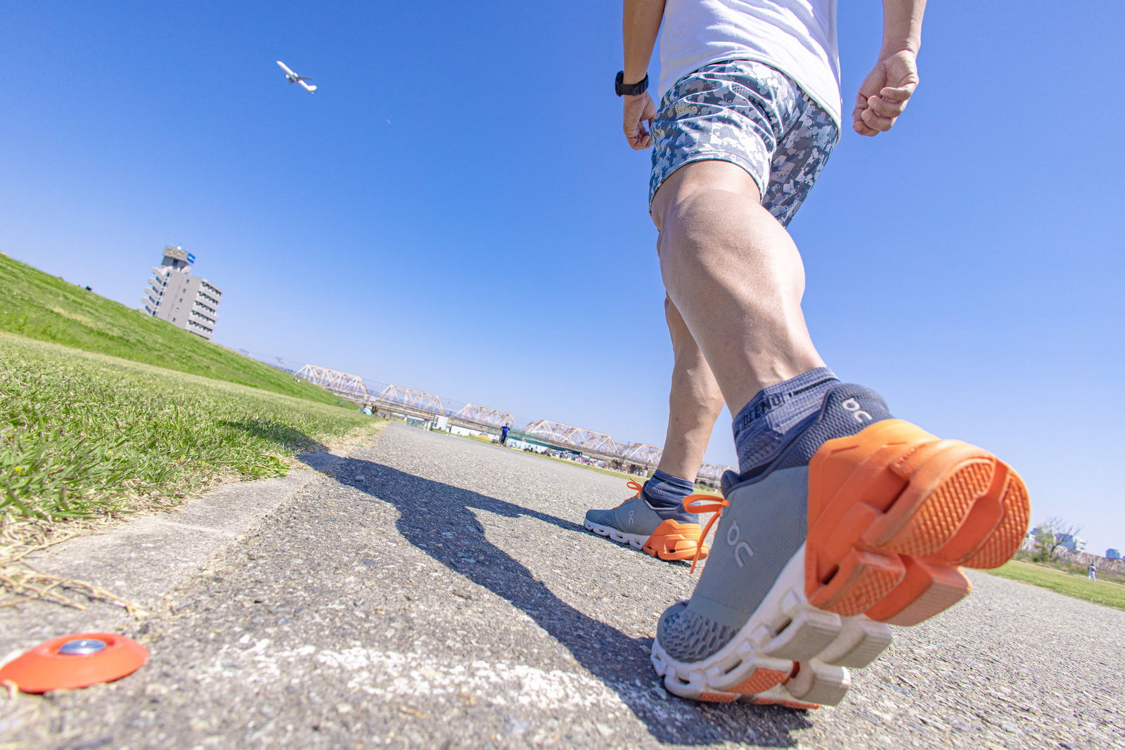 オレンジ色のランニングシューズでアキレス腱を伸ばす男性の足元［モデル：うえせい］