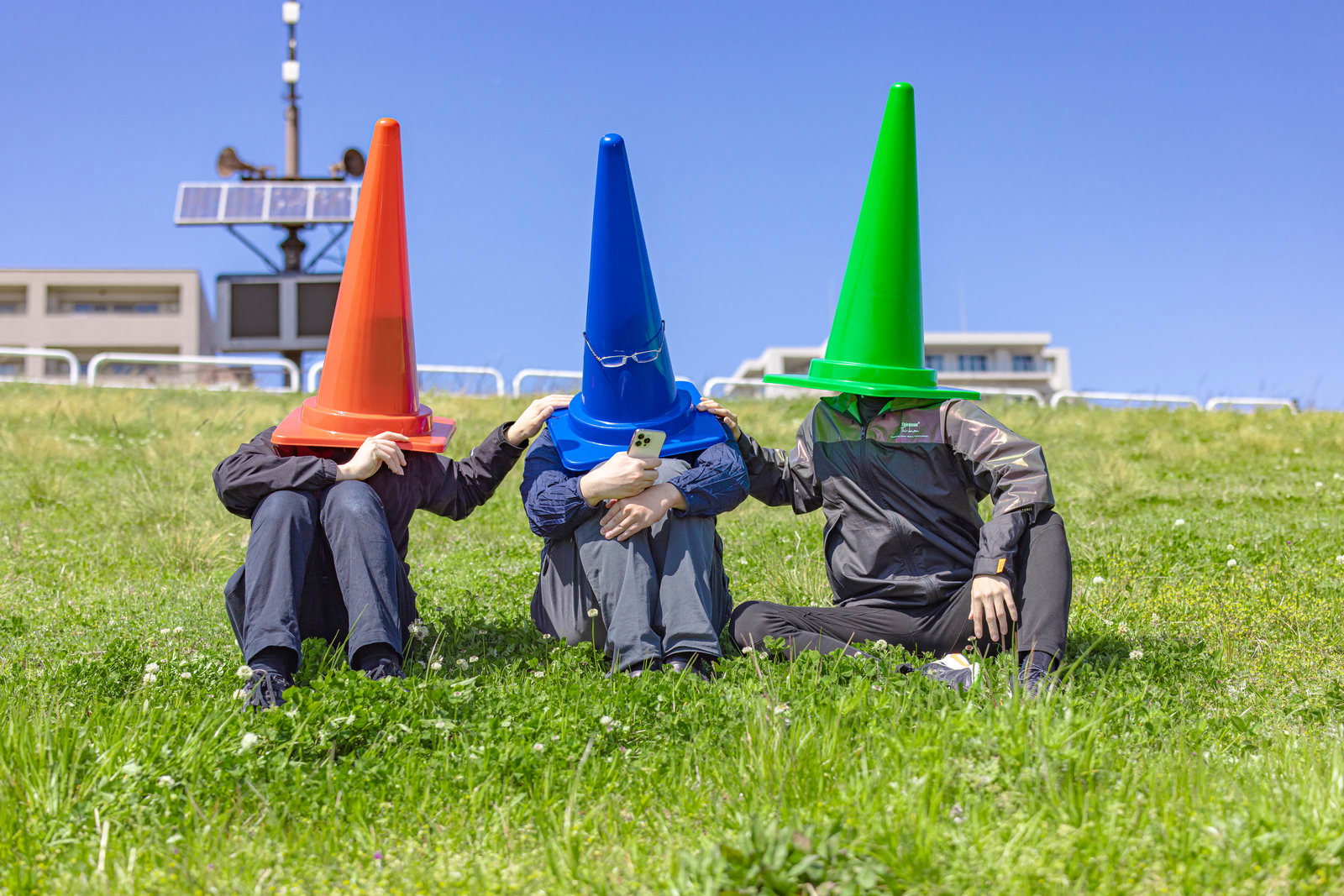 草原で座り込むカラーコーンを頭にかぶった3人の人物