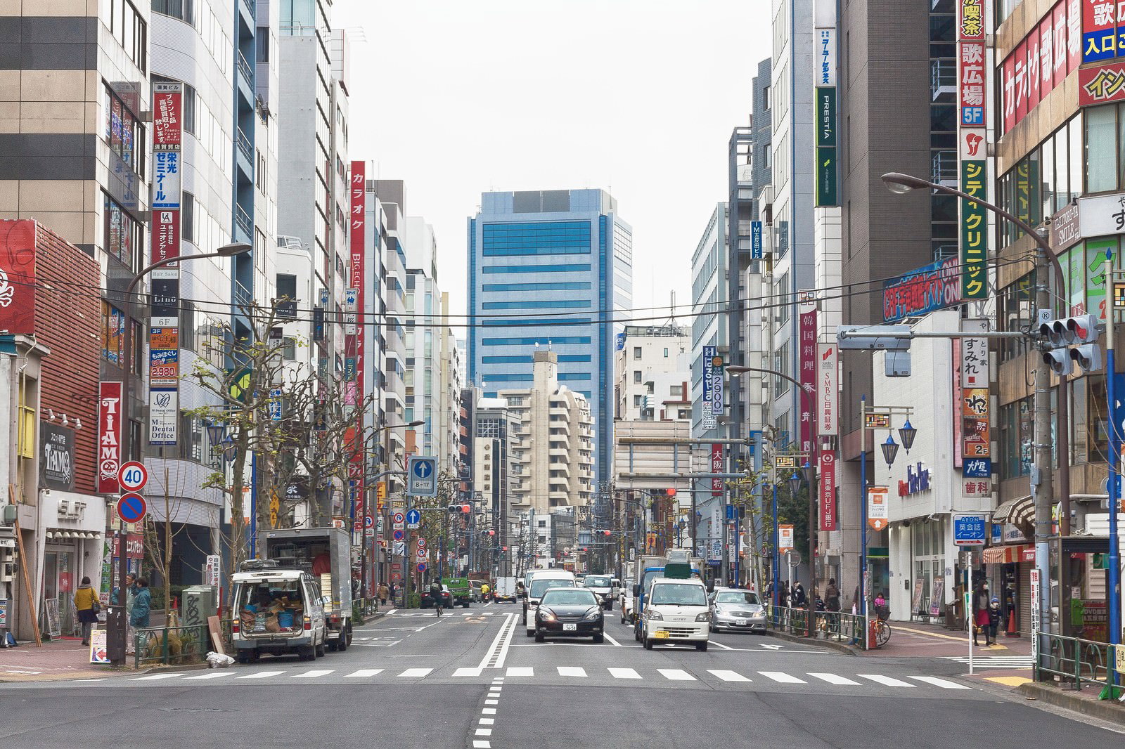 五反田駅前の繁華街で、看板が並ぶビルの間を横断歩道で横切る人と車