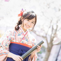 桜の満開の花と卒業証書を持った袴姿の女性の写真