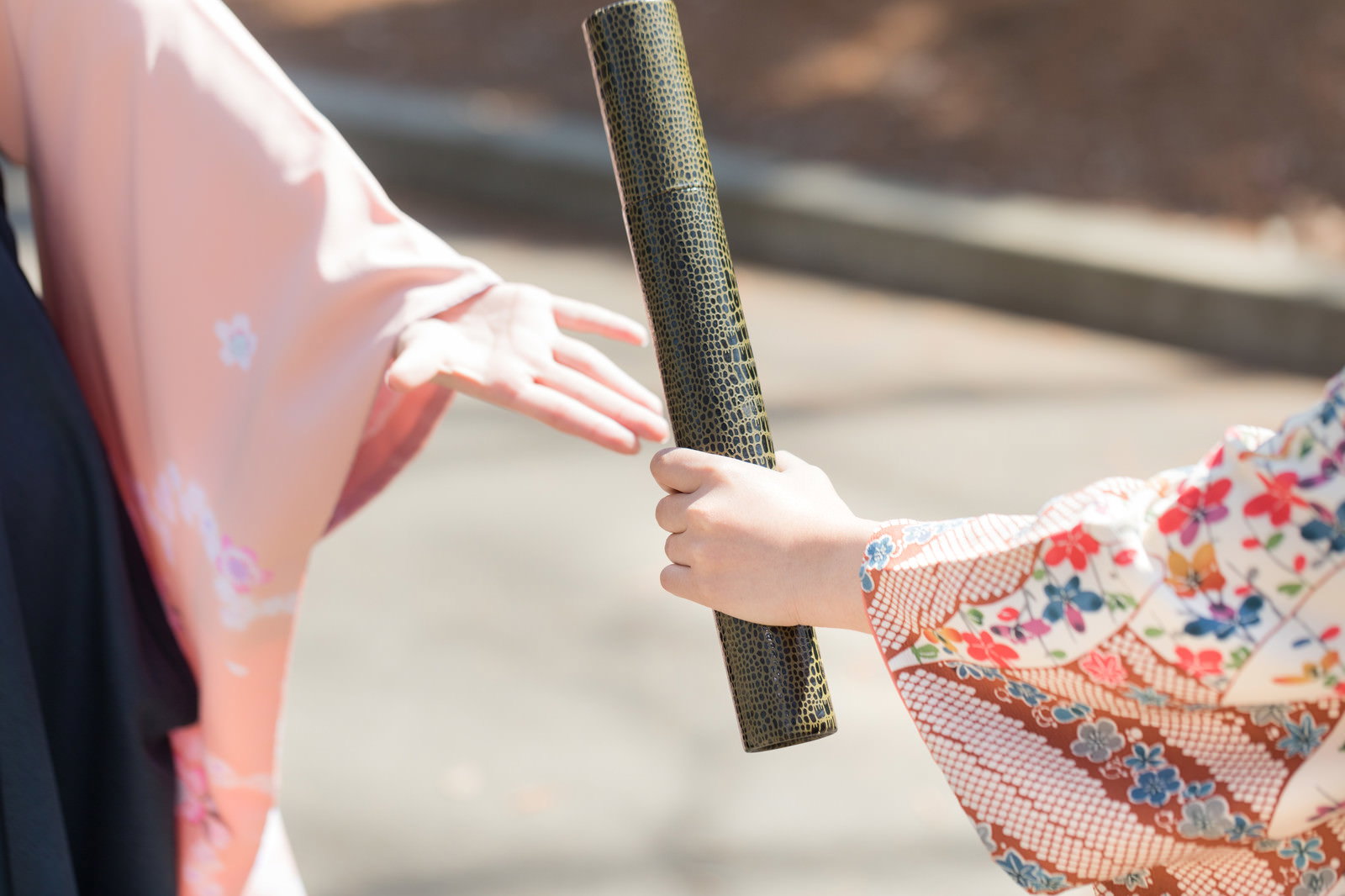 着物を着た女性が卒業証書の筒を手渡ししている様子