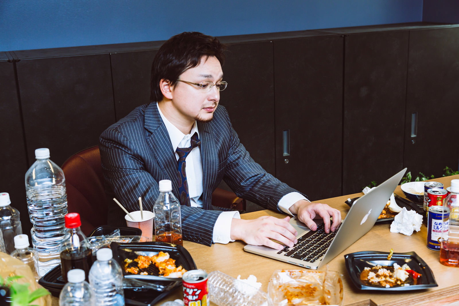 散らかったデスクでノートパソコンを操作するスーツ姿の男性［モデル：Max_Ezaki］