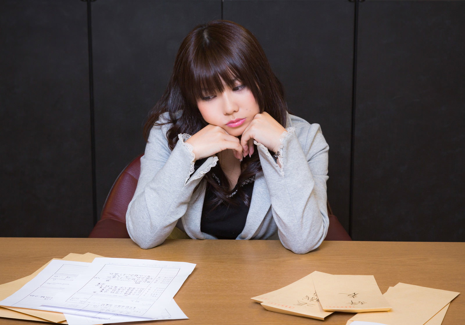 机に向かって頬杖をつき困った表情を浮かべるグレースーツの女性［モデル：Lala］