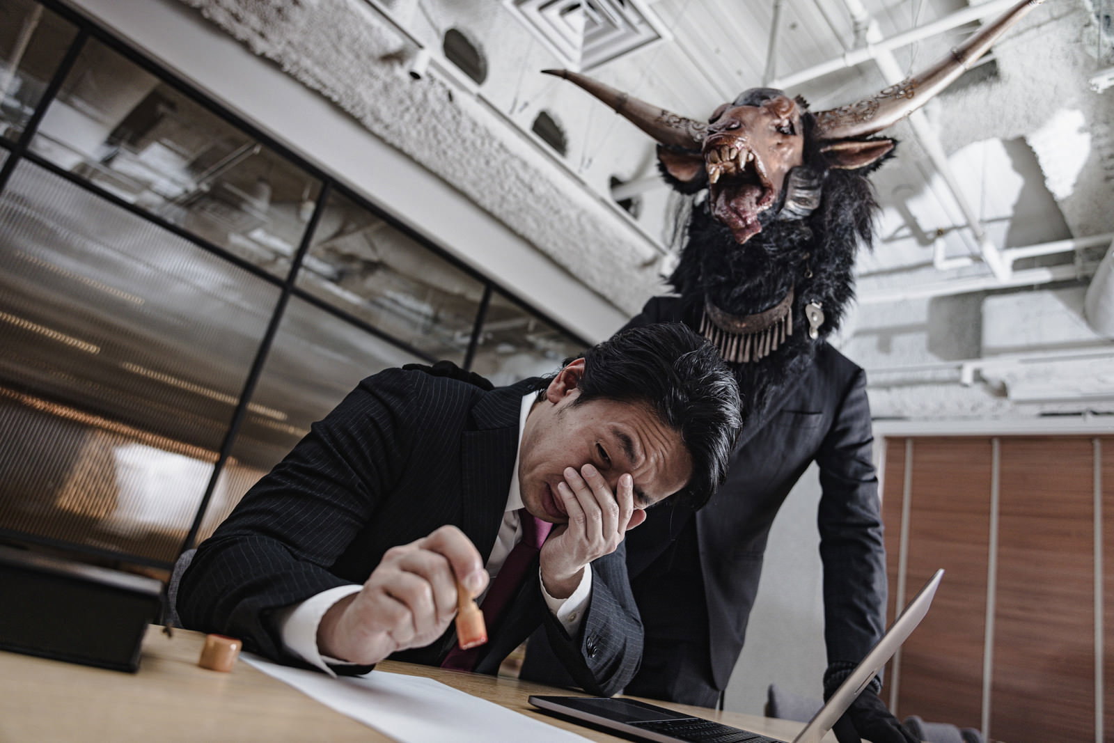 契約書に判子を押そうとするスーツ姿の男性と背後に立つ悪魔