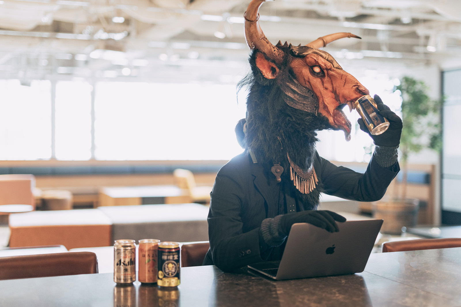 オフィスで缶ビールを飲む魔神マスクの人物