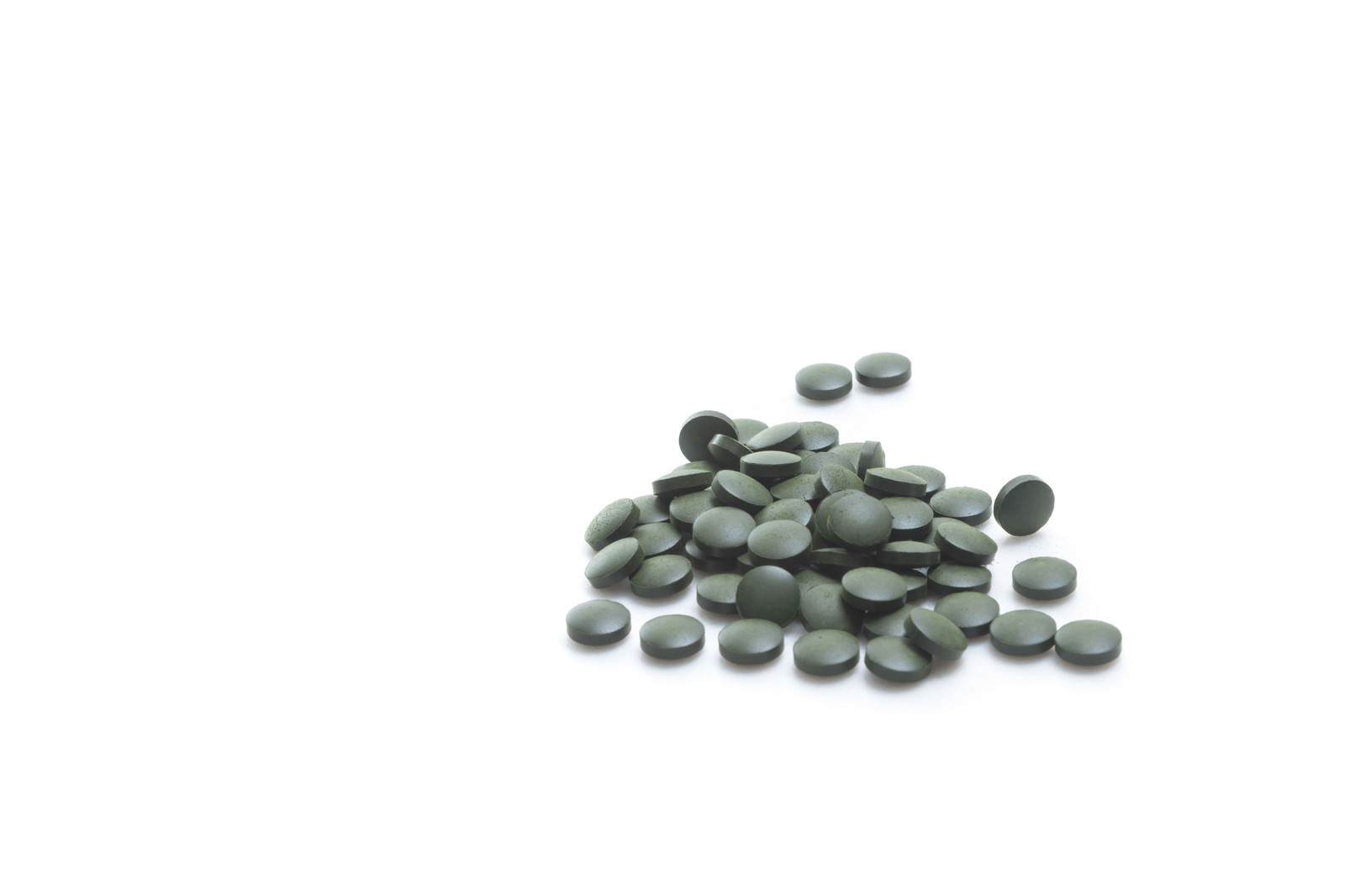 Green Spirulina tablets scattered on a white background