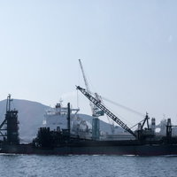 長崎県の港に停泊するフェリーの後姿と海砂採取船の写真