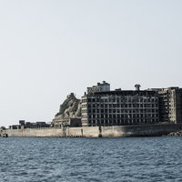 船から見る軍艦島の廃墟建物群（端島保育園跡・70号棟端島小中学校跡）の写真