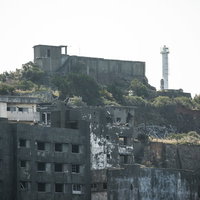 軍艦島にそびえる肥前端島灯台、廃墟群を背にした白いコンクリート造りの写真