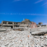 端島炭鉱総合事務所跡越しの肥前端島灯台（軍艦島）の写真