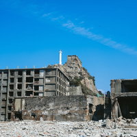 第三見学広場から見る肥前端島灯台と崩壊建物（軍艦島）の写真