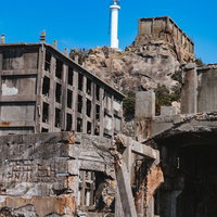 高台に聳え立つ肥前端島灯台と廃墟建物群（軍艦島）の写真