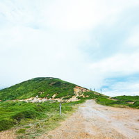 毛無峠頂上から鉄塔方面を望む山岳風景と未舗装路の写真