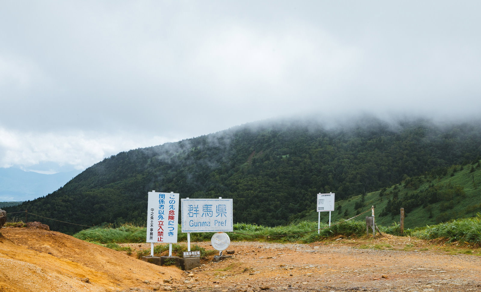 曇り空の下、緑の山々を背景に設置された毛無峠の立入禁止警告看板