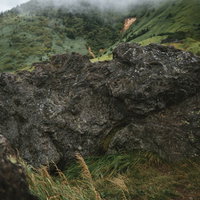 毛無峠の緑の草原に点在する大きな岩石と山々の風景の写真