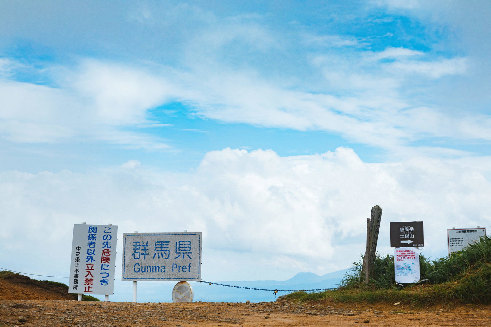 青空の下、毛無峠に設置された立入禁止の警告看板と荒涼とした大地