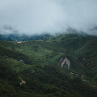 強風が吹き抜ける毛無峠の霧立ちこむ渓谷と山道の景観の写真