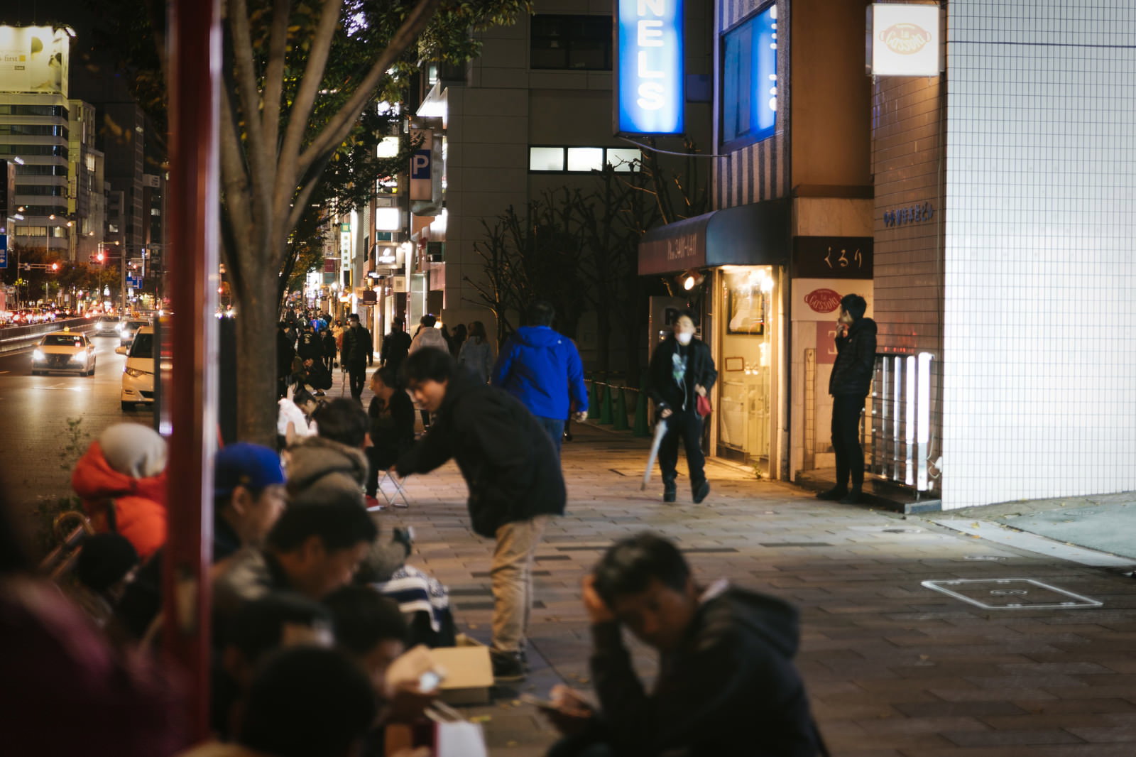 夜の歩道に座り込んで並ぶ多くの人々の長蛇の行列