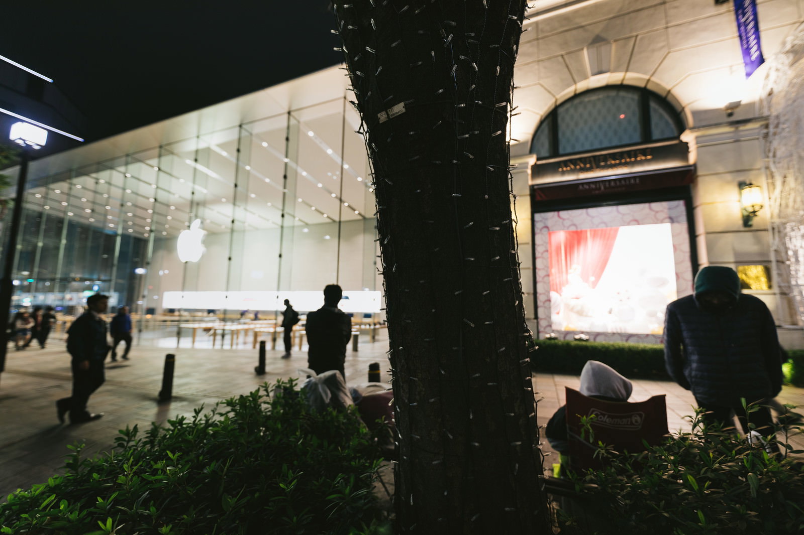 夜のアップルストア前の歩道に並ぶ長い行列と店舗の明るいショーウィンドウ