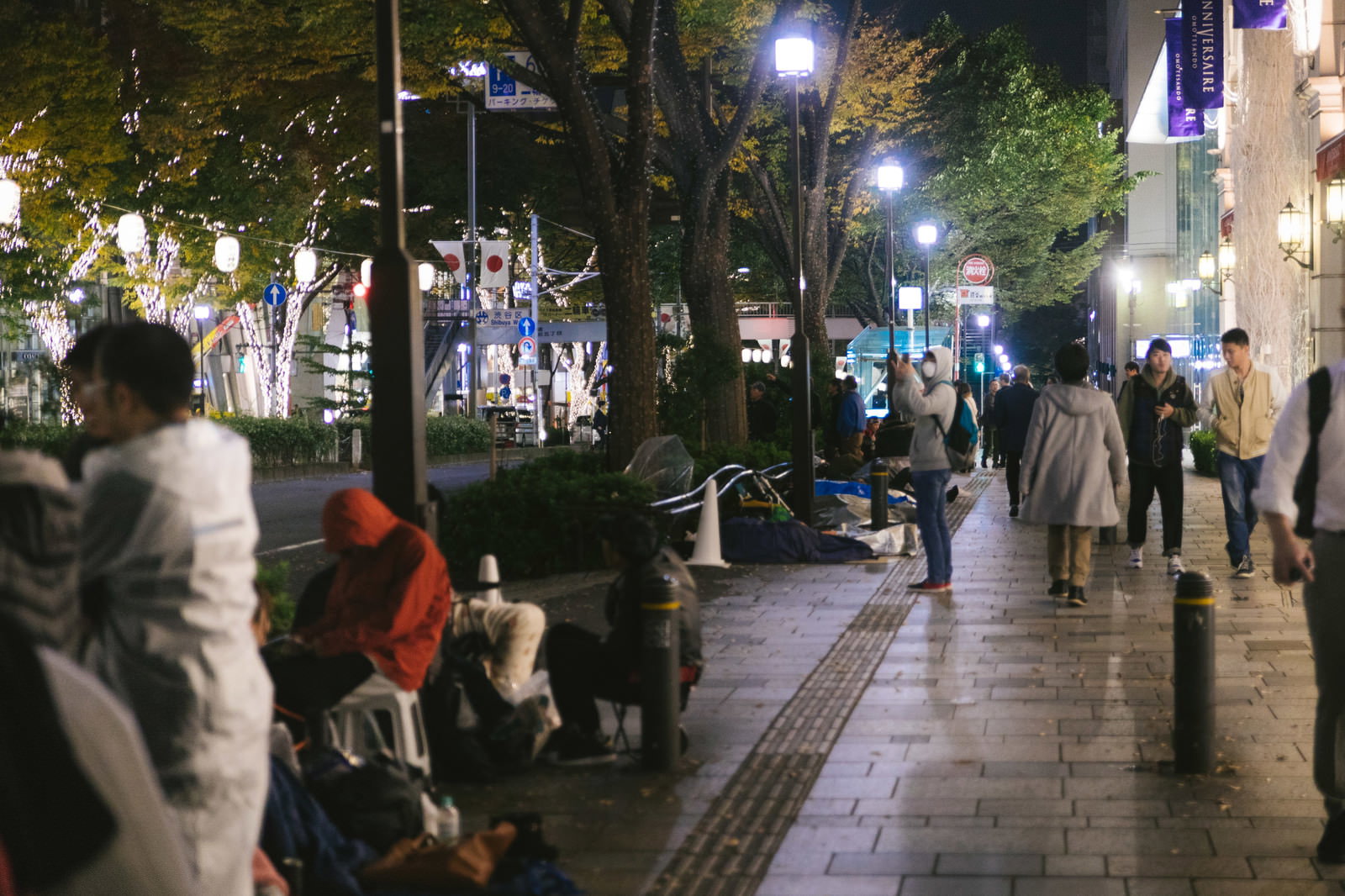 夜の街で歩道に座り込んで列を作る多くの人々