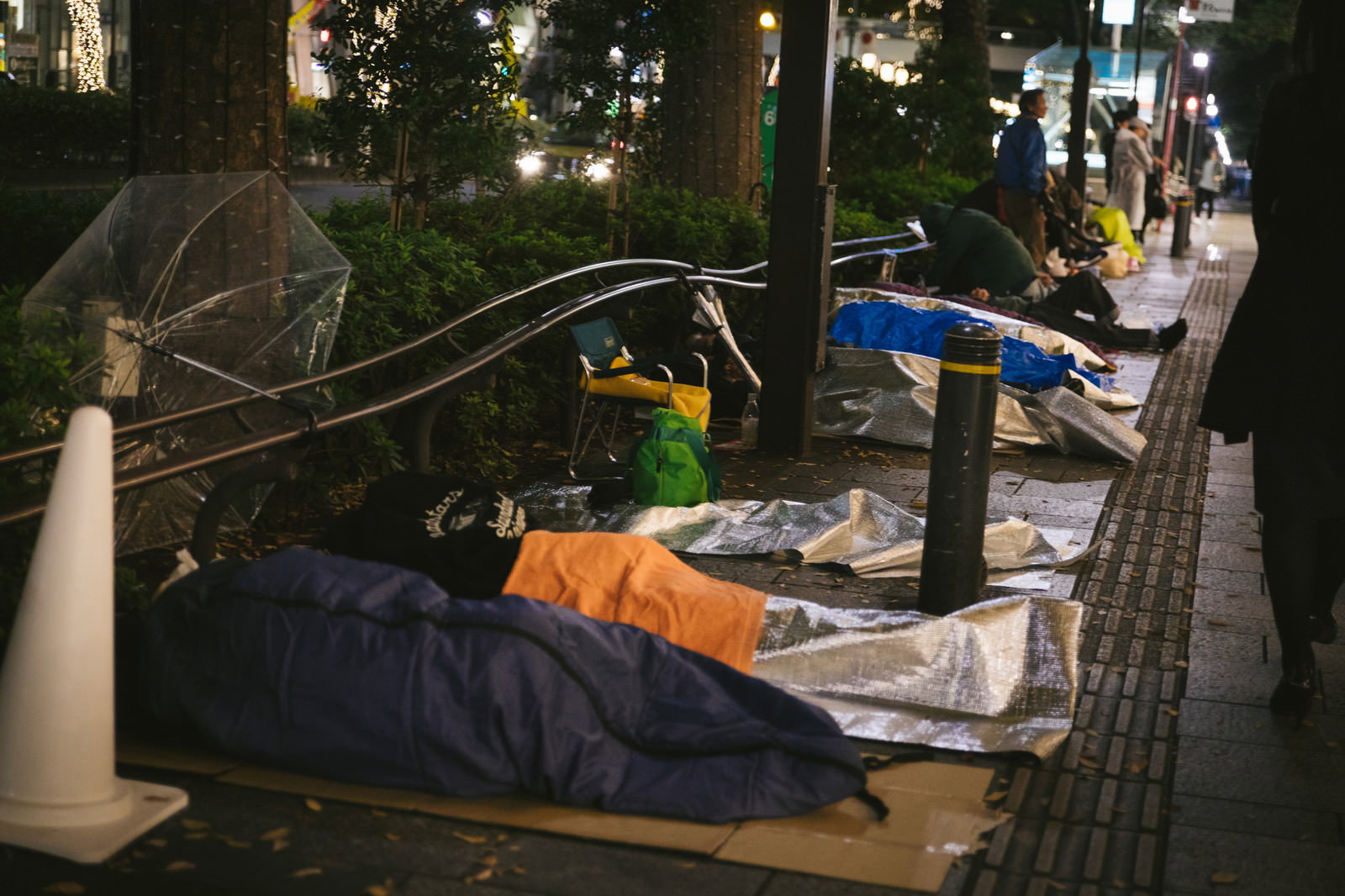 歩道で寝袋を使って徹夜行列に並ぶ人々