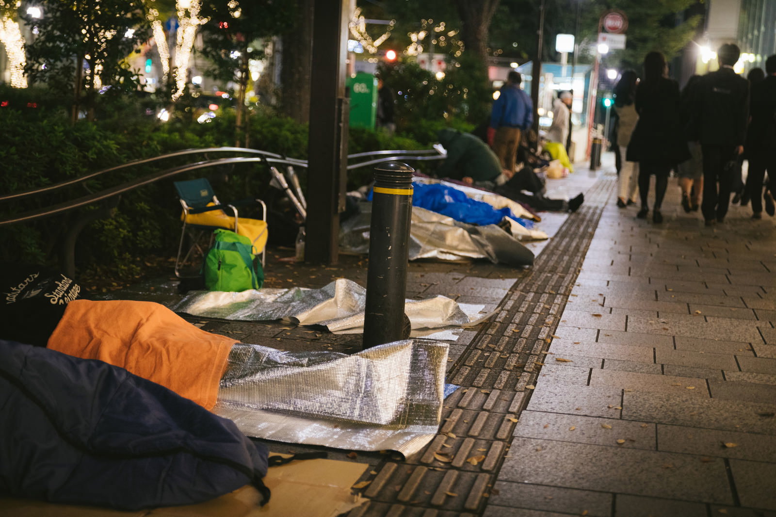 新製品発売前夜に歩道で寝袋を並べて待つ人々