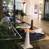 店舗前の歩道に寝袋を敷いて並ぶ徹夜行列の待機風景の写真