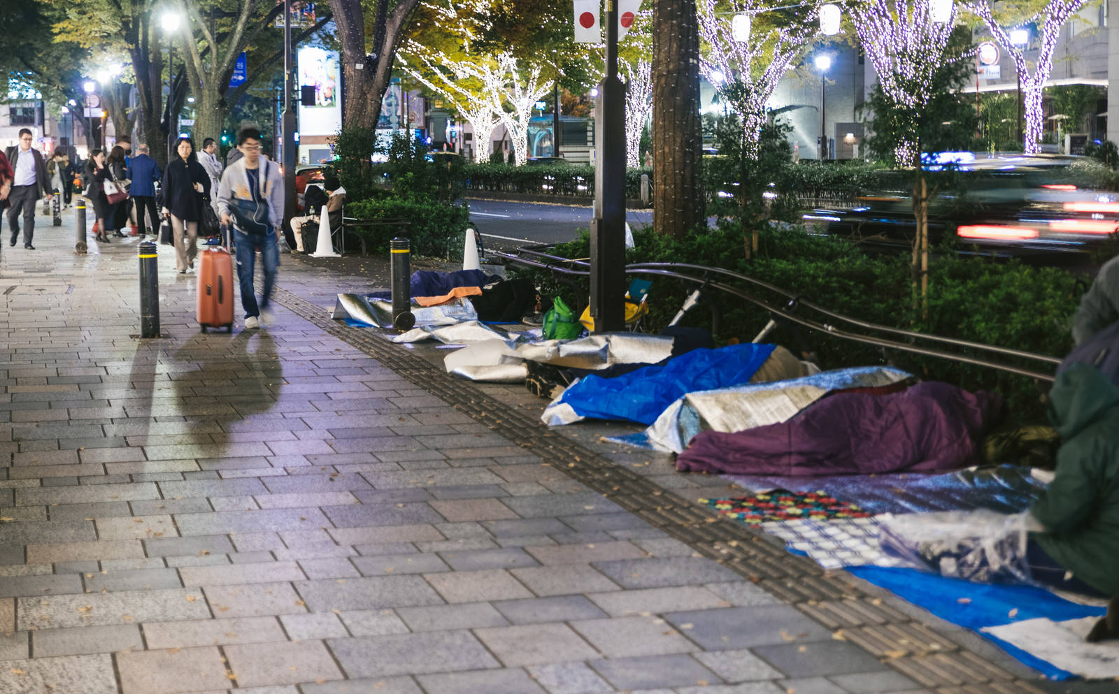 歩道に青い寝袋を敷いて並ぶ徹夜行列の人々