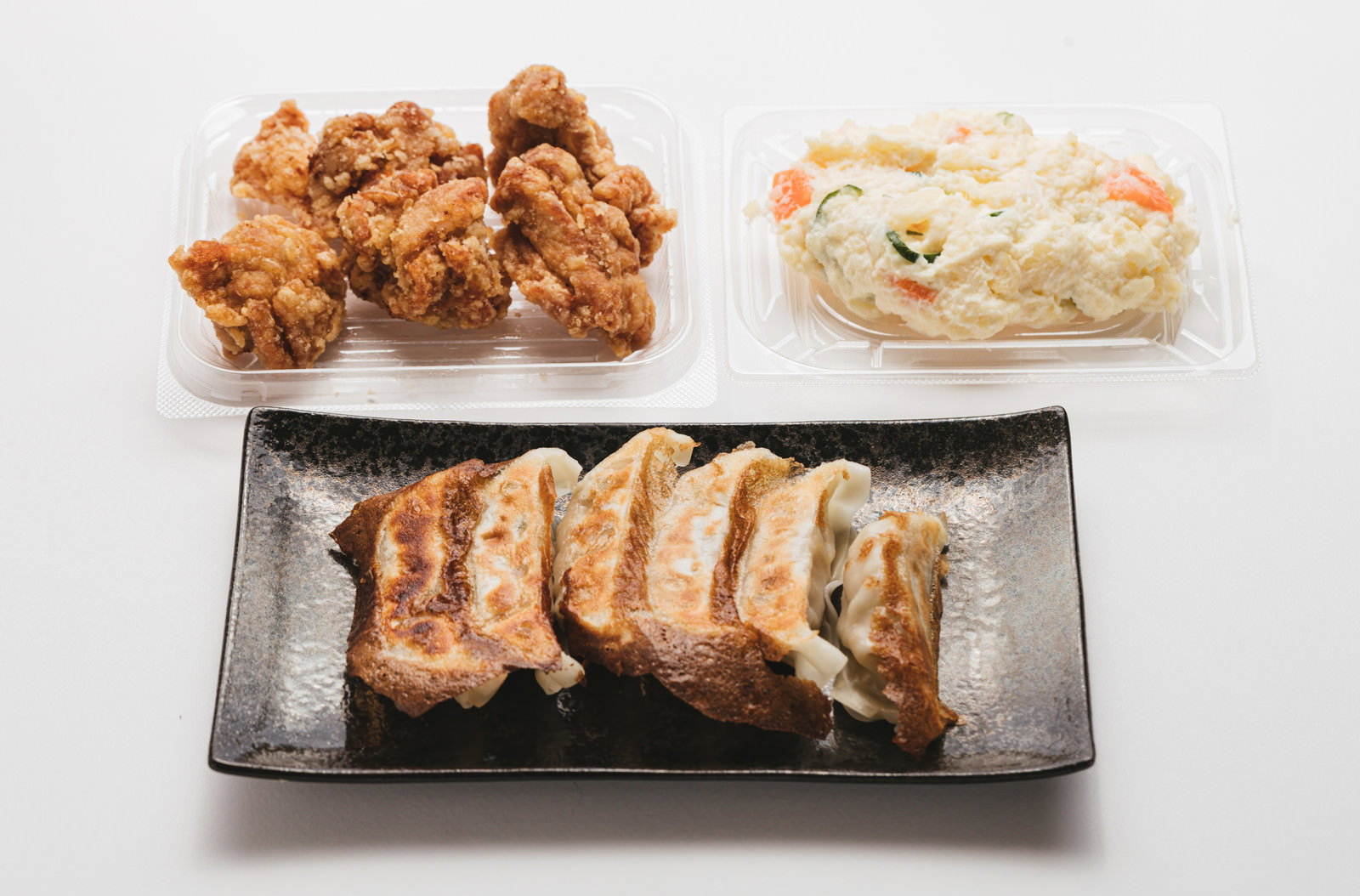 茶色い皿の唐揚げ、白い容器のポテトサラダ、黒い皿の餃子が並ぶ