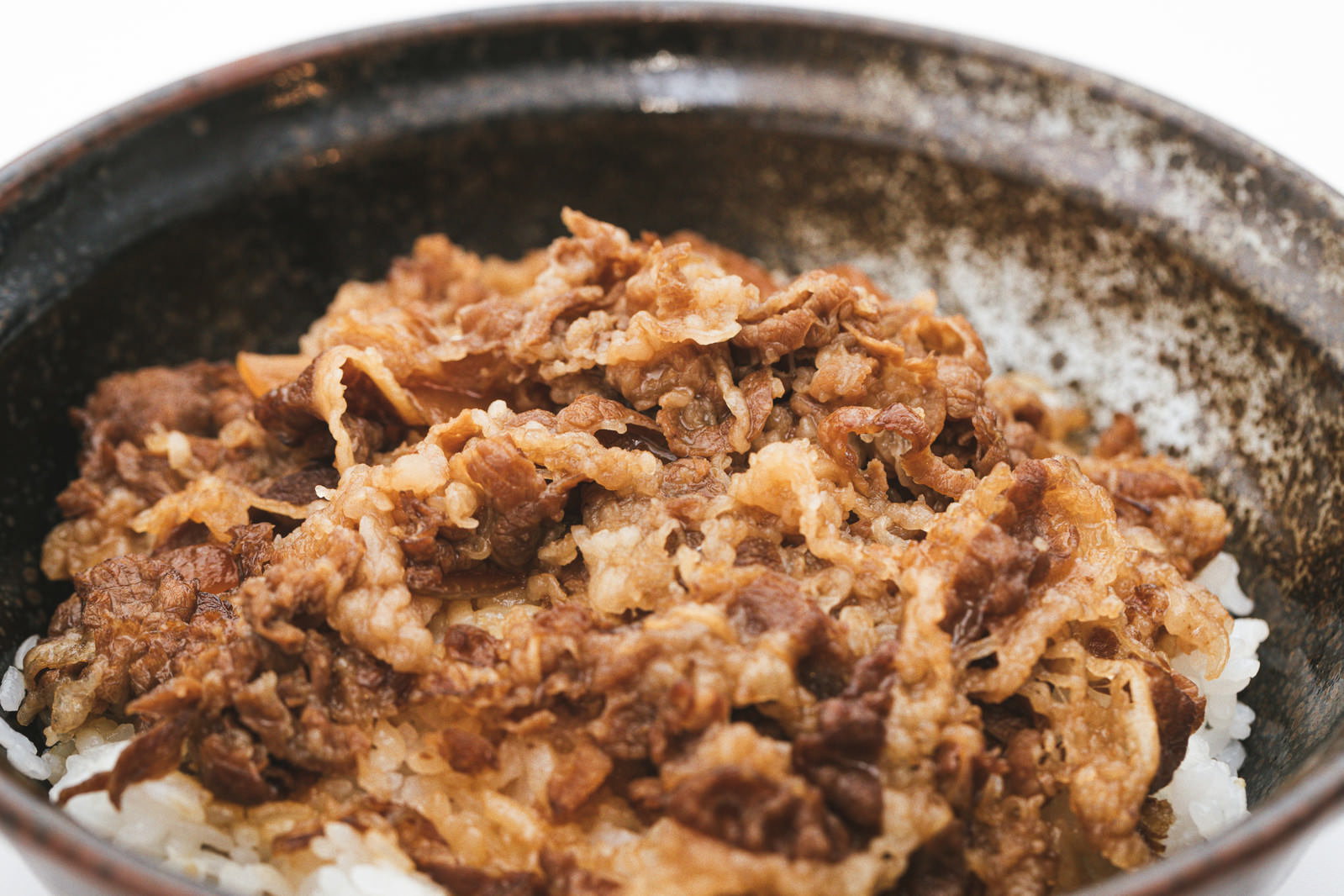 茶色い陶器の丼に盛られた牛丼。白いご飯の上に煮込んだ牛肉と玉ねぎ
