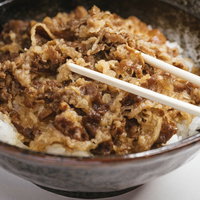 白い箸で食べる牛丼、甘辛く煮込んだ牛肉と玉ねぎがのった和食の丼の写真