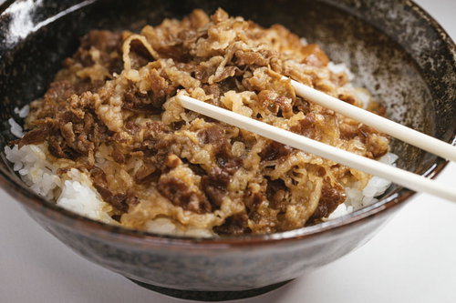 白い箸で食べる牛丼、甘辛く煮込んだ牛肉と玉ねぎがのった和食の丼