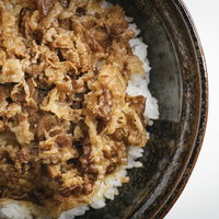 黒い丼に盛った牛めし一人前、牛肉と玉ねぎの甘辛煮込みの写真