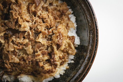 黒い丼に盛った牛めし一人前、牛肉と玉ねぎの甘辛煮込み