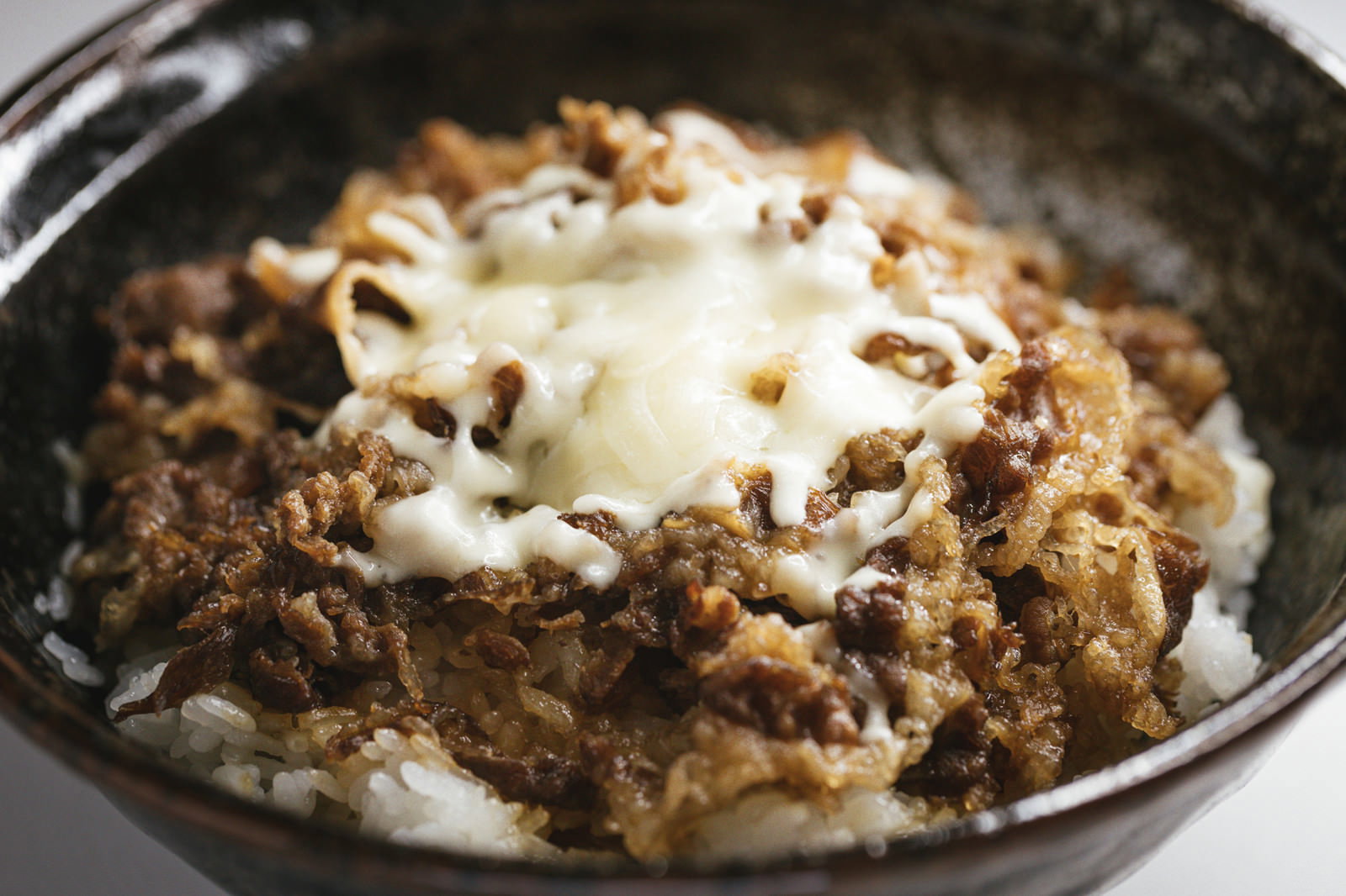 黒い丼に盛られた牛丼の上に白いとろけるチーズがかかっている
